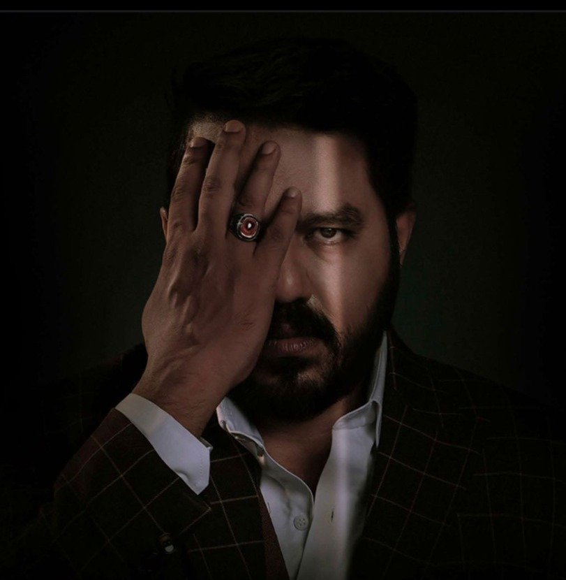 Mentalist Aathi, one eye revealed behind his hand, in dramatic low light